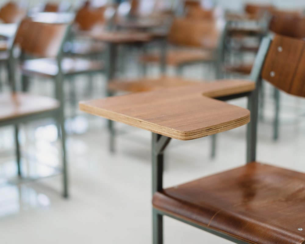 Empty university classroom with many wooden chairs. Wooden chairs well arranged in college classroom. Empty classroom with vintage tone wooden chairs. Back to school concept.